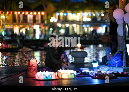 Vietnam, Hoi An. Une vieille dame qui vendait des lanternes flottantes à côté de la rivière Thu bon dans le centre-ville. Banque D'Images