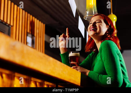 Red-haired woman élever son doigt tout en appelant le barman Banque D'Images