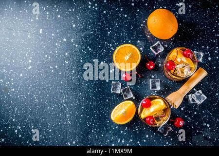 L'alcool classique cocktail, whisky avec des glaçons, des tranches d'orange et cocktail de cerise rouge. Dans deux verres, sur une table en béton, bleu foncé Banque D'Images