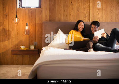 Couple reading book et using digital tablet in bed Banque D'Images