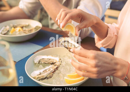 Femme avec manucure soignée squeezing jus de citron sur les huîtres fraîches Banque D'Images