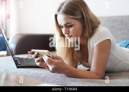 Attractive young woman relaxing sur un canapé à la maison et à l'aide d'un écran tactile smart phone pour socialiser et réseau d'accueil Banque D'Images