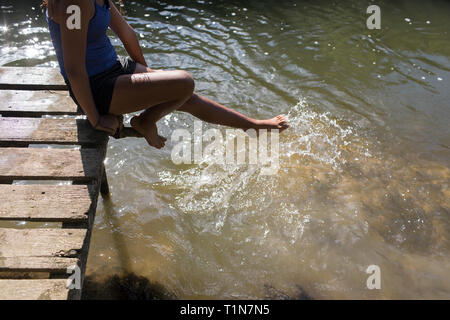 Fille sur le quai ensoleillé pied éclaboussures dans l'eau de la rivière Banque D'Images