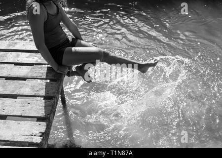 Playful girl splashing pieds à sunny river Banque D'Images