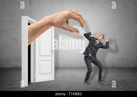 Man in suit couvrant la tête avec les mains pour se protéger de l'énorme main émergeant de la porte. Banque D'Images