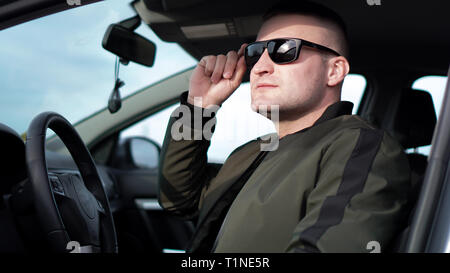 Vue latérale du jeune homme élégant, confiant dans les lunettes de soleil au volant de sa voiture Banque D'Images