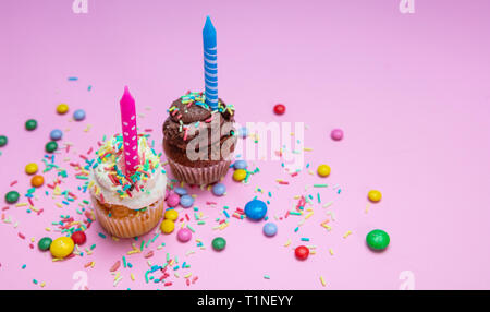 Garçon et fille d'anniversaire. Deux cupcakes vanille et chocolat avec des bougies sur rose pastel arrière-plan, copiez l'espace. Banque D'Images