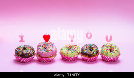 Valentines Day. Mini cakes avec du glaçage coloré et saupoudre sur fond rose, texte je t'aime Banque D'Images