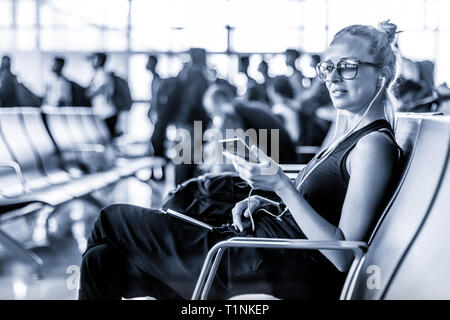 Female traveler en utilisant son téléphone portable en attendant de monter à bord d'un avion à l'embarquement au terminal de l'aéroport d'Asie. Libre photo en noir et blanc. Banque D'Images