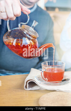 Processus de préparation du thé, une tasse de thé fraîchement infusé de fruits rouges et de miel. Le thé chaud verse de l'électrique dans la tasse. Banque D'Images