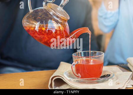 Processus de préparation du thé, une tasse de thé fraîchement infusé de fruits rouges et de miel. Le thé chaud verse de l'électrique dans la tasse. Banque D'Images