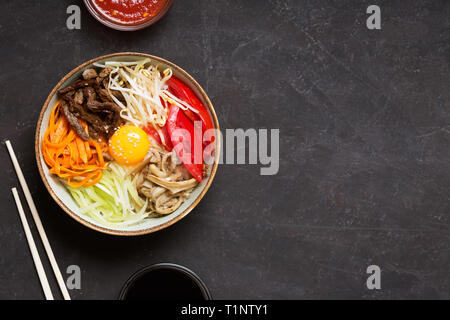 Plat de riz coréen bibimbap. Généralement servi comme un bol de riz blanc chaud avec des légumes et des oeufs. Fond noir, vue du dessus Banque D'Images