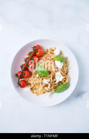 Les pâtes spaghetti à la chapelure, de la mozzarella, basilic frais et un plant de tomates dans une assiette blanche avec un fond clair. Avec un plat de pâtes italiennes Banque D'Images