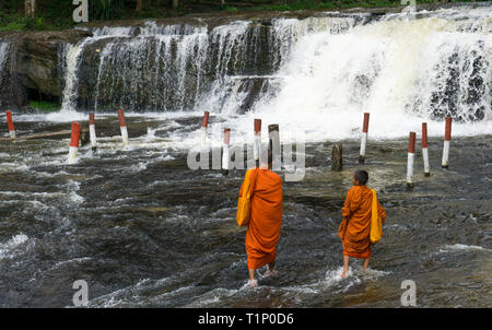 Deux jeunes moines bouddhistes marcher en eau peu profonde vers une chute d'eau Banque D'Images