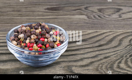 Mélange de poivre. Noir, blanc, vert et rouge poivre corns. Bol en verre sur fond de bois. Piper nigrum. Mélange d'assaisonnement sec close-up. Banque D'Images