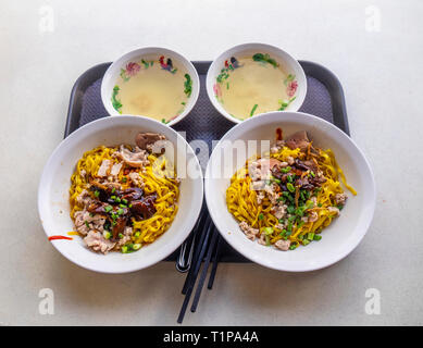 Plateau avec petit-déjeuner traditionnel singapourien deux bols de nouilles aux champignons et de porc haché et 2 petits bols de bouillon. Singapour. Banque D'Images