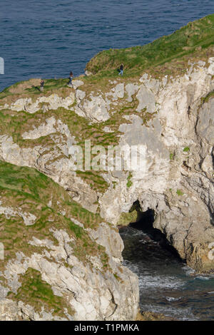 Les jeunes gens qui marchent le long d'un étroit chemin falaise mer sur une arche en pierre calcaire à Kinbane Head, dans le comté d'Antrim, en Irlande du Nord. Banque D'Images