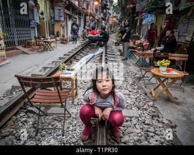 Curieux fille vietnamienne accroupis sur des rails et regarde dans la caméra dans la rue de la ville de Hanoi, Vietnam Banque D'Images