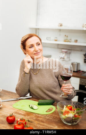 Transmission d'une bonne lady holding verre de vin tout en se penchant sur la table Banque D'Images