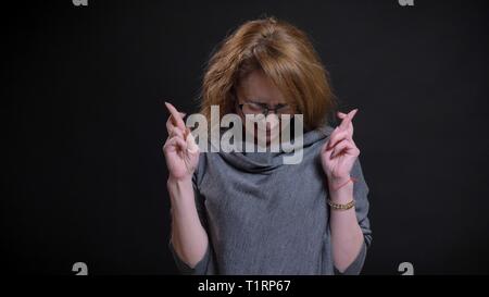 Closeup portrait of middle-aged femme rousse extravagante dans les verres d'avoir ses doigts croisés dans l'espoir et prier avec impatience Banque D'Images