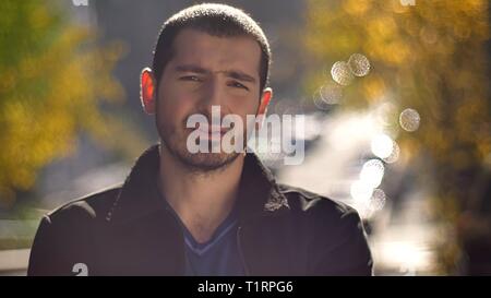 Portrait of caucasian man watching sérieusement en huis clos et le clignotement sur la rue d'automne arrière-plan. Banque D'Images