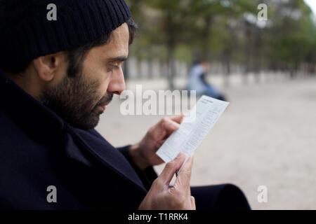 L'homme d'origine pakistanaise, indienne, d'origine asiatique, assis dans city park, reading leaflet - hiver Banque D'Images