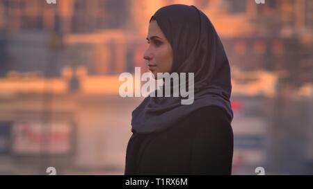 Vue côté gros plan portrait de jeune femme en hijab attrayant à tout droit à l'appareil photo avec urban city sur l'arrière-plan Banque D'Images