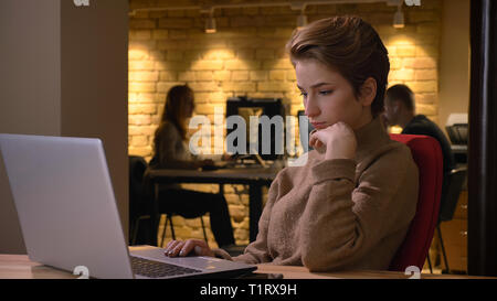 De jeunes pousses closeup portrait of attractive female office worker typing sur l'ordinateur portable à l'intérieur sur le lieu de travail Banque D'Images