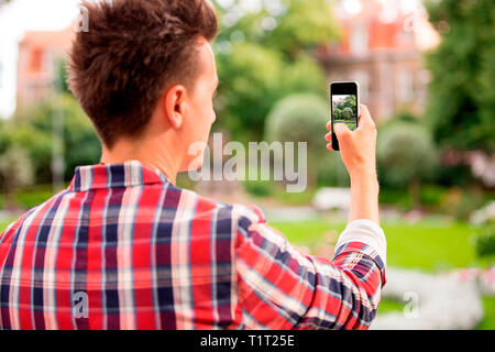 L'homme prend une photo avec téléphone intelligent. Photo de beau bâtiment avec jardin fleuri, touristique. Banque D'Images