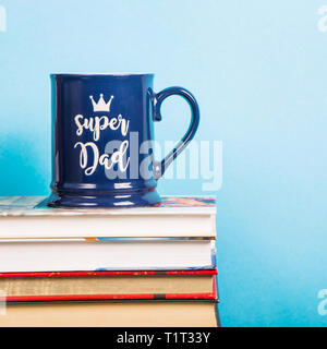 Tasse bleu avec l'inscription super papa sur une pile de livres sur le bleu de l'arrière-plan. Copy space Banque D'Images