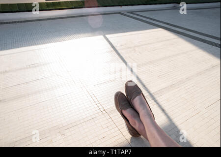 Une femme au repos les pieds et les chevilles, à la recherche dans le soleil, entouré par l'espace négatif. Banque D'Images