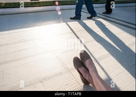 Une femme se détend dans le soleil du soir tandis que les passants par projettent de grandes ombres. Banque D'Images