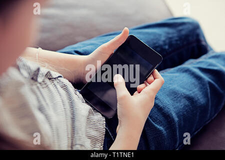 Au cours de l'épaule d'un enfant à l'aide d'un smartphone dans un environnement d'accueil Banque D'Images