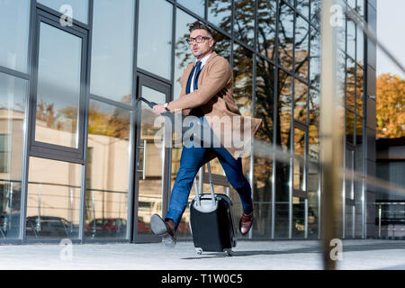 Handsome businessman en costume et enduire d'exécution avec valise et parapluie sur street Banque D'Images