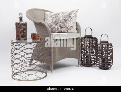 Wicker Chair et coussins avec une petite table et deux porte-bougie en osier sur un fond blanc Banque D'Images