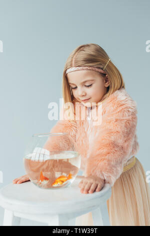 Adorable gamine dans un manteau en fausse fourrure et à la jupe à fishbowl sur tabouret isolé sur gray Banque D'Images