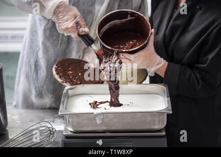 Les mains dans les gants femmes la préparation de crème glacée au chocolat - ganache au chocolat verser dans le bac en acier inoxydable Banque D'Images