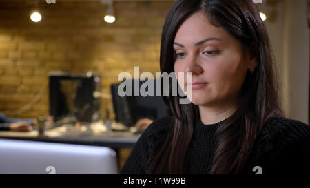 Portrait de belle femme d'âge moyen de l'embonpoint à regarder attentivement dans l'ordinateur portable sur l'arrière-plan du bureau. Banque D'Images