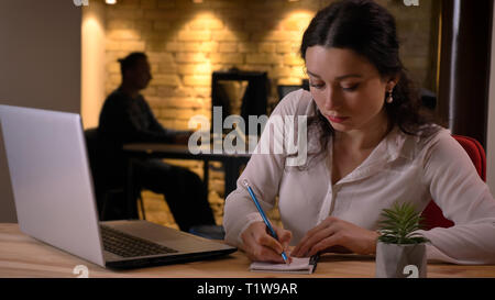 De jeunes pousses Gros plan pretty caucasian businesswoman typing sur l'ordinateur portable et la prise de notes à l'intérieur sur le lieu de travail Banque D'Images