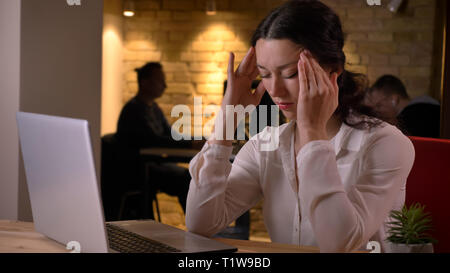 De jeunes pousses Gros plan pretty caucasian businesswoman having a headache tout en tapant sur l'ordinateur portable à l'intérieur sur le lieu de travail Banque D'Images