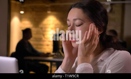 De jeunes pousses Gros plan jolie femme employée ayant un mal de tête tout en tapant sur l'ordinateur portable à l'intérieur sur le lieu de travail Banque D'Images