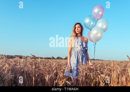 Belle jeune fille se tient en été dans un champ de blé. Dans sa main une femme détient des ballons. Reste après le week-end, un groupe et un anniversaire dans la nature. Long Banque D'Images