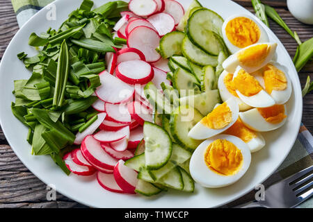 Salade de printemps frais verts, œufs durs, de radis et de concombre servi sur une plaque blanche sur une table en bois rustique, vue horizontale de abov Banque D'Images