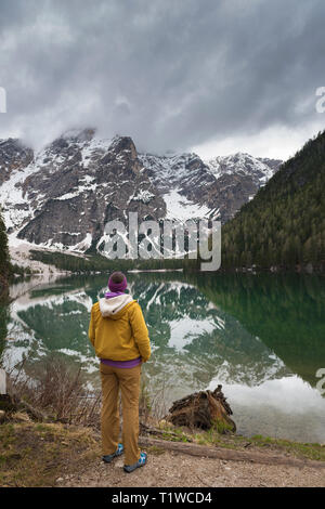 Une brunette woman randonneur, portant l'équipement de plein air est debout en voyant la vue sur le lac de Braies. Golden et arbres verts représentent l'automne. Banque D'Images