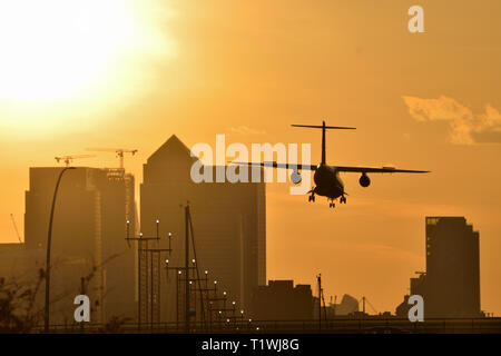 Avion à l'atterrissage à l'aéroport de London City avec un ciel d'or que le soleil se couche derrière les toits de Canary Wharf Banque D'Images