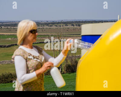 A mature woman pulling une bouteille en plastique dans un bac en plastique jaune pour recyclage Banque D'Images