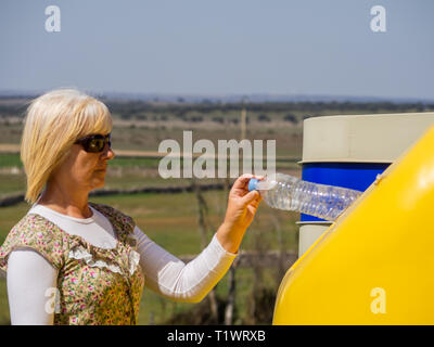 A mature woman pulling une bouteille en plastique dans un bac en plastique jaune pour recyclage Banque D'Images