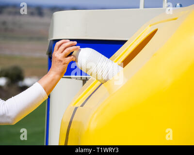 A mature woman pulling une bouteille en plastique dans un bac en plastique jaune pour recyclage Banque D'Images