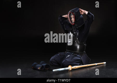 Le kendo fighter sitting on floor and taking off casque sur noir Banque D'Images