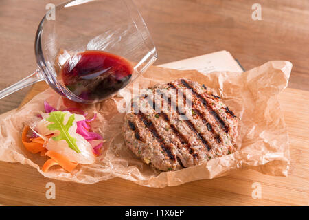 Des boulettes de porc servi dans un papier recyclé sur une planche de bois avec un verre de vin rouge. Banque D'Images